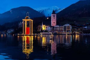 Floating lantern in front of St. Wolfgang, with the Weißes Rössl and snow-covered Schafberg in the evening.