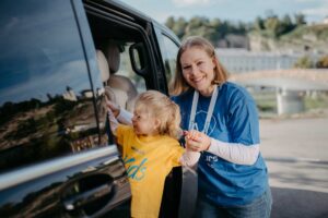 A young child, donning a bright "Kids" t-shirt, is helped into a minivan by a smiling guide from weTours, showcasing the family-friendly nature of the Private Sound of Maria Tour.
