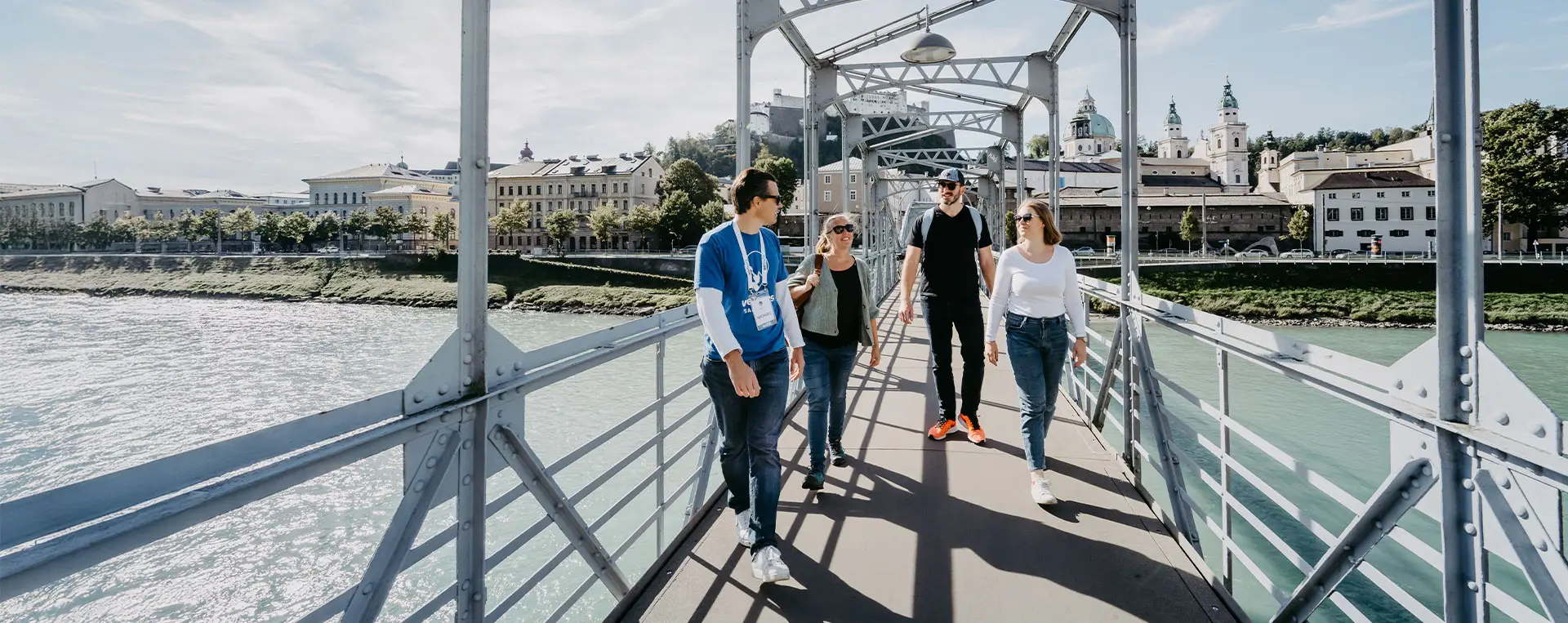 Tour group with guide crossing Mozart Footbridge with Salzburg’s Old Town in the background